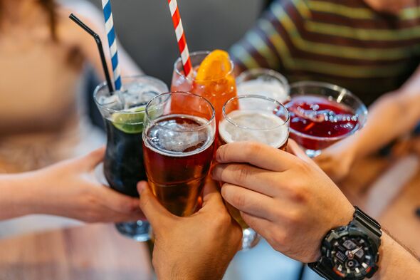 A group of young friends is relaxing in a bar, cheering with their alcoholic drinks (cocktails and beer).