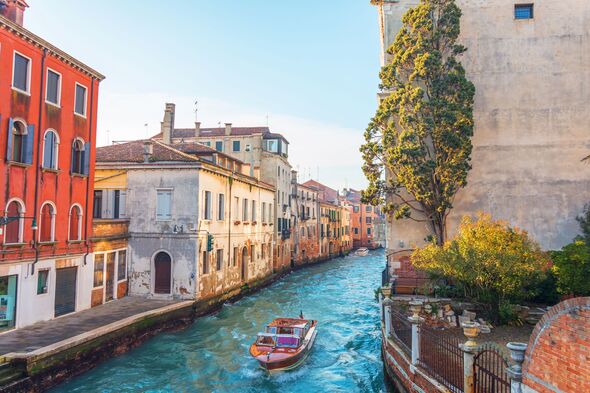Canal in Venice with a small garden and a tree near the house, on the water a small motor boat.