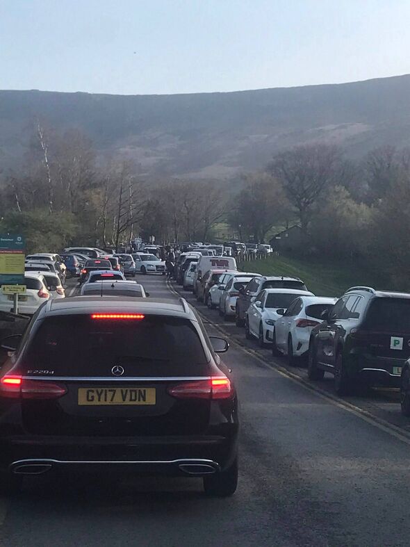 An image depicting a substantial traffic congestion on a two-lane highway. Numerous vehicles, including SUVs and sedans, are par