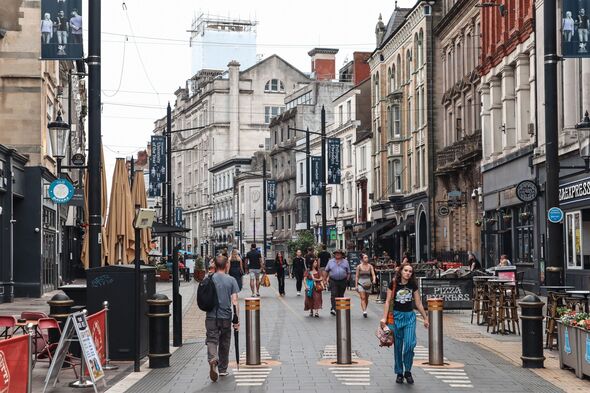 Busy pedestrian street with people walking among historic buildings and cafes in central Cardiff