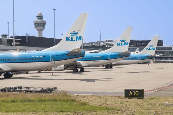 Three KLM airline planes in a row at Amsterdam Schiphol Airport with the control tower in the background.