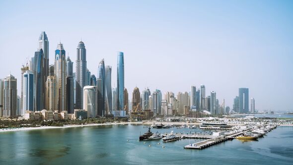 Skyscrapers rise high in Dubai along the waterfront with boats docked nearby during clear weather