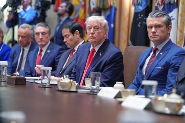 A group of formally dressed individuals, presumably in a professional setting, are seated around a conference table. Various ite