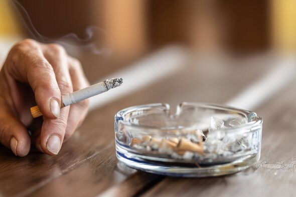 The hand of a smoking woman with a cigarette taps the ash into an ashtray.
