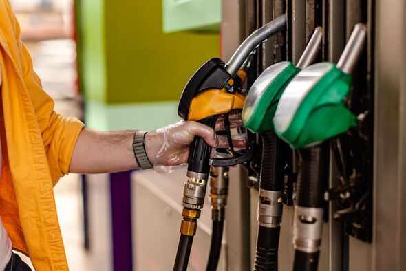 Driver uses fuel pump at a gas station to refuel a vehicle during day time in an urban area
