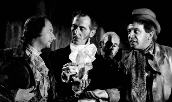 A black-and-white photograph depicts a group of individuals standing together, engaged in conversation. The person in the center