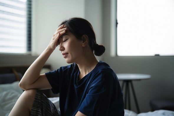 Young Asian woman with eyes closed resting on bed feeling headache. Exhausted woman with her hand on head not feeling well. Woman in pain. Concepts of