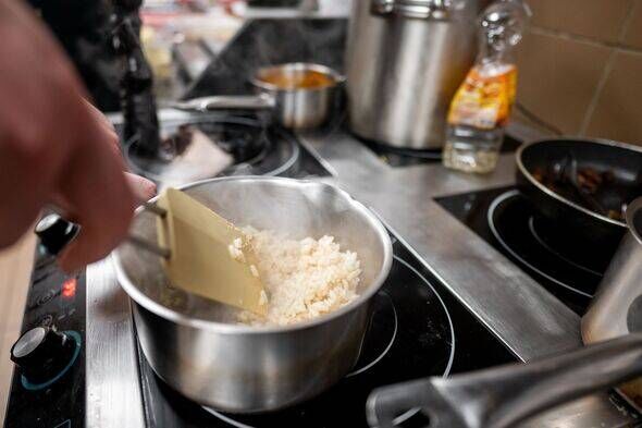 A cook stirs rice in a steaming pot on a modern stovetop. Various cooking utensils and pots are present, creating an inviting at