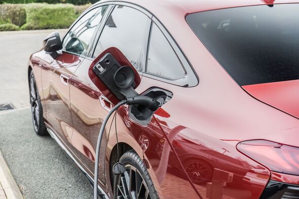A close-up of a red Audi A6 getting charged by a plug