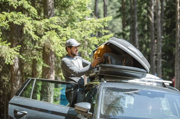 Man filling cargo box container on roof rack for camping vacation.