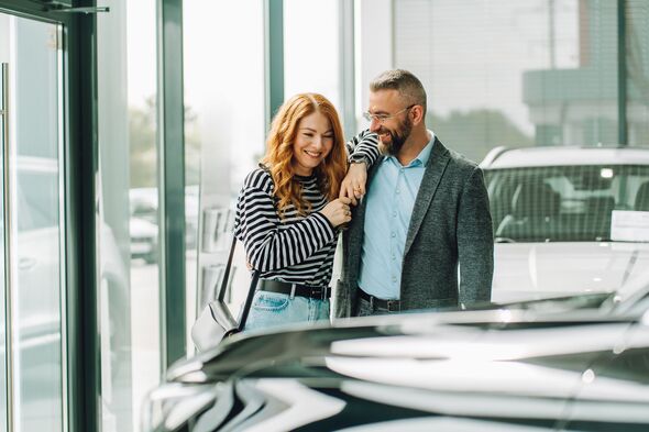 New car choosing. Happy couple looking for new vehicle in dealership showroom