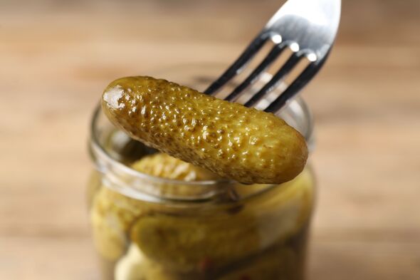 Eating tasty pickled cucumber at table, closeup