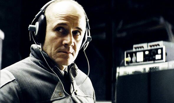 Bald man in a grey jacket wearing large headphones