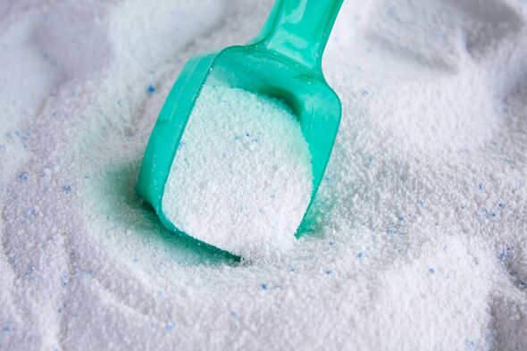 A close-up image displays a teal-colored plastic scoop filled with a white powdery substance. The powder appears to be uniformly