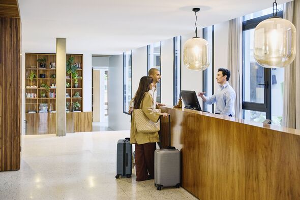 Wide shot tourist couple checking in at hotel reception desk