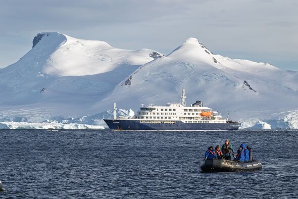 MV Hondius cruise ship sailing in Antarctica with snow-capped mountains and icebergs, zodiac expedition boat with tourists exploring the icy waters an