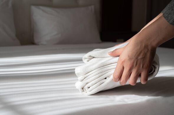 Hands making bed in hotel room.