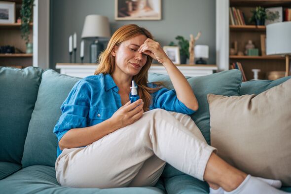 Sick woman using nasal spray at home on sofa