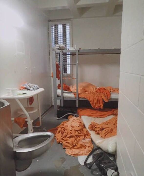 An image of a small dormitory room with bunk beds. The lower bed appears to be made, while the upper bed is disheveled with scat