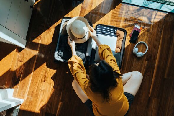 Overhead view of young Asian woman sitting on the floor in her bedroom, packing a suitcase for a trip. Getting ready for a vacation. Traveller's acces