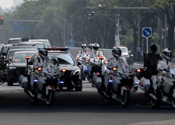 An image depicting a convoy of motorcycles and vehicles traveling along a road, with several individuals wearing helmets. The sc