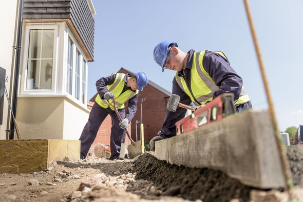 Apprentice builders using digger to lift kerb stones on housing building site
