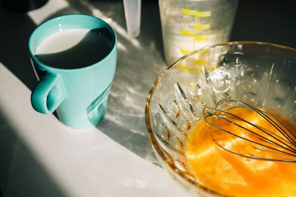 Whisking eggs and preparing ingredients on a sunlit kitchen counter, featuring a glass bowl, milk cup, and measuring jug.