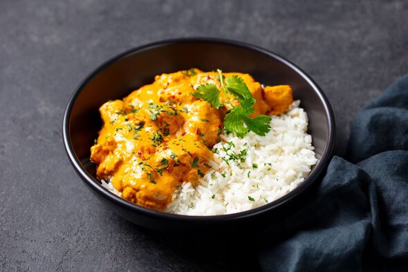 Creamy chicken curry over fluffy white rice, garnished with fresh cilantro. Grey background. Close up.