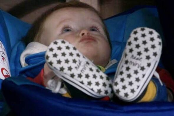 An infant, likely resting in a stroller, is dressed in a colorful outfit and wears matching polka-dot patterned shoes. The baby
