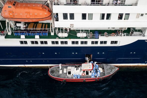 Health service personnel assisting patients onto a boat from MV Hondius
