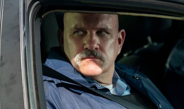 Man with moustache looking out of a car window.