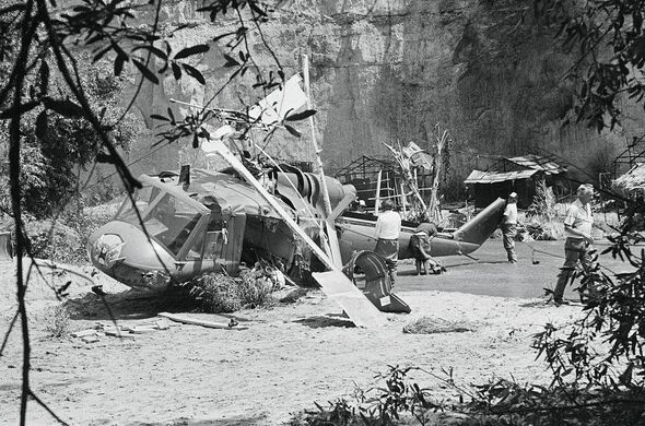 The black-and-white photograph depicts a chaotic scene of individuals working amidst a forest setting. Some individuals are seen