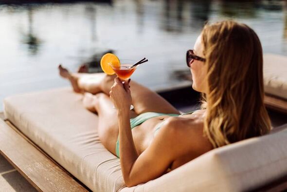Woman relaxing by the pool at summer sitting on a sunbed drinking cocktail