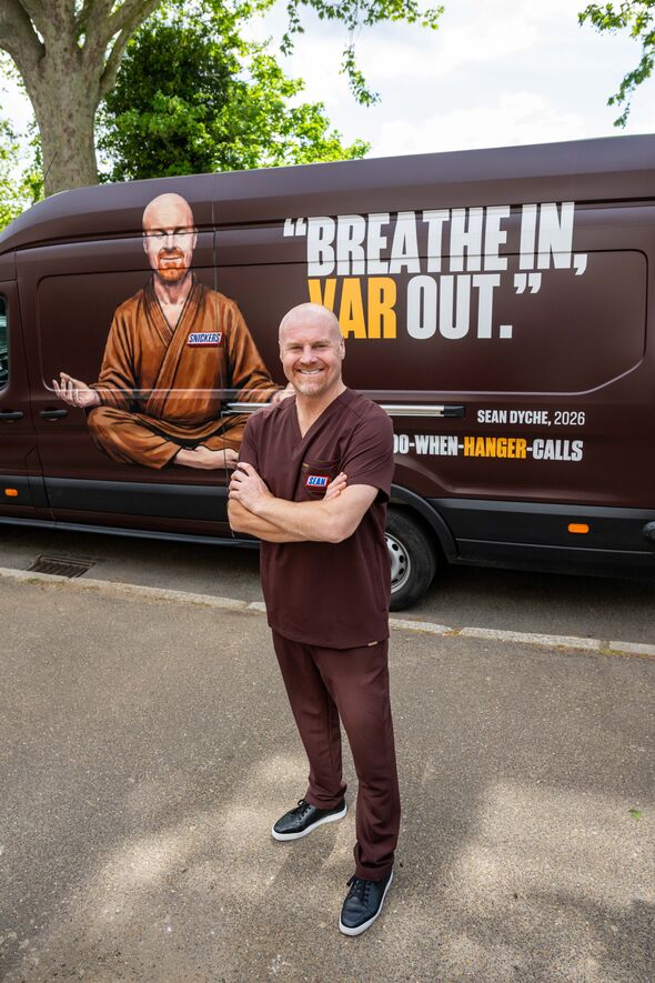 Sean Dyche stands in front of a van with arms crossed smiling. The van reads 'Breathe in, VAR out'.