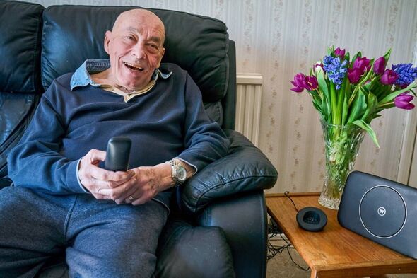 John Garrad sits on his sofa at home