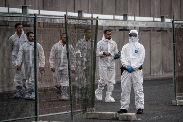 A group of individuals dressed in protective white suits and masks are standing in a secured area, possibly engaged in an invest