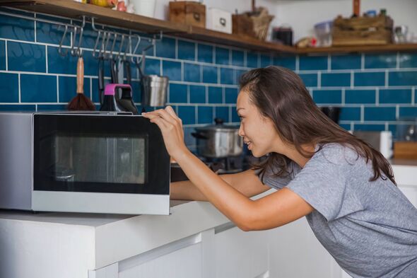 Side shot of a beautiful Asian woman opening her microwave to checking her meals that reheated.