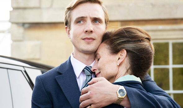 Young blonde man in dark blue suit hugs a smiling middle-aged woman