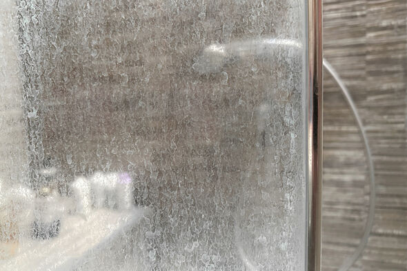 dirty shower glass door with white mineral residue from hard water and soap scum.