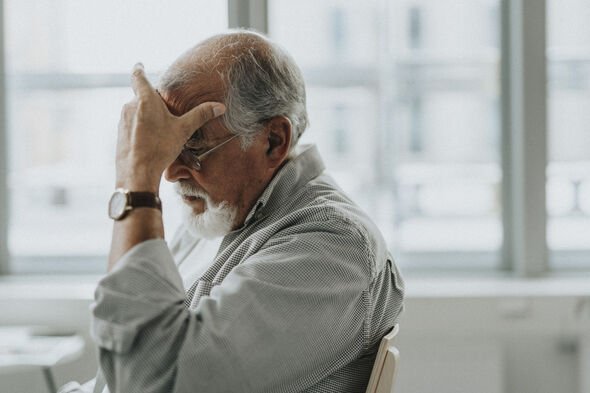 Stressed senior male patient sitting with head in hand at healthcare center