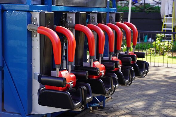 A series of red and black ride seats are attached to a blue structure, possibly for a roller coaster or a similar amusement park