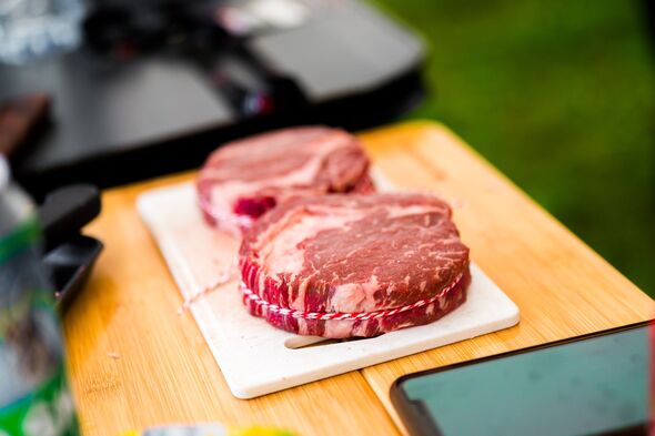 A perfectly trimmed and trussed raw ribeye steak sits on a wooden cutting board with a metal skewer, prepared for high-stakes professional grilling at