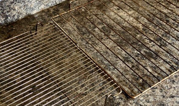 An image of a metallic grill with a rectangular shape positioned on a stone surface. The grill is composed of parallel metallic