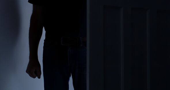 Silhouette of a man opening a door to a dark room he stands in the doorway clenched fist.