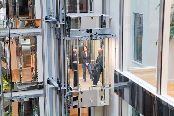 Two businessmen and a businesswoman talking in a glass elevator in a modern building in Paris