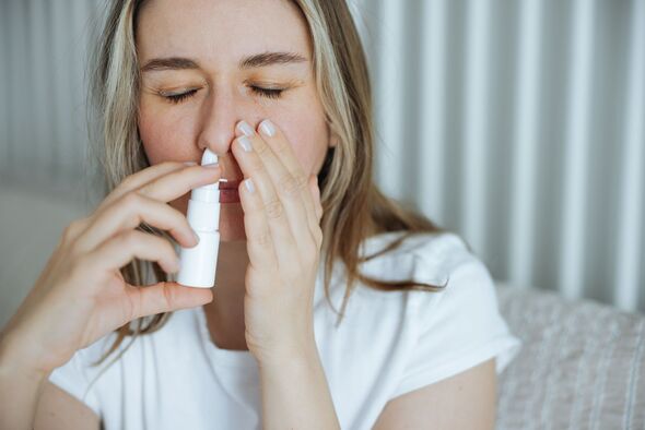 Sick young woman using nasal spray