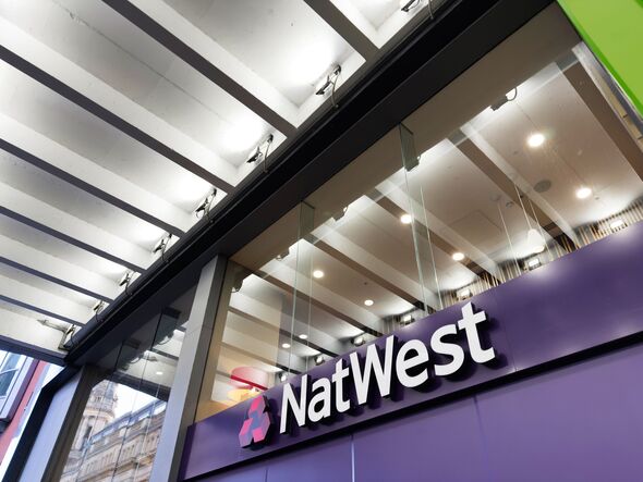 Exterior of NatWest bank branch in Manchester UK with modern glass facade and purple signage under lit canopy