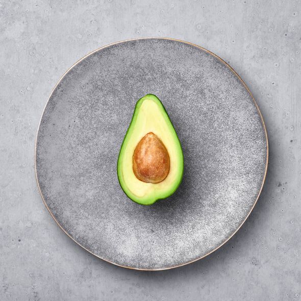 Half Avocado in gray hand made matte plate on concrete rough backdrop. Grey ceramic saucer setting.