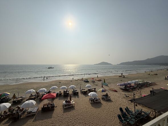 Image of busy sandy beach view from beach hut cottage balcony, white wood railing, rows of sun loungers and parasols, sunny clear blue sky and sea bac