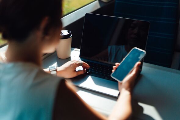 Over the shoulder view of young Asian businesswoman using smartphone and laptop in train